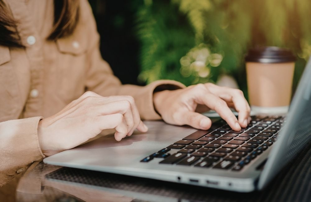 Close-up of hands typing on a laptop at a desk with plants in the background