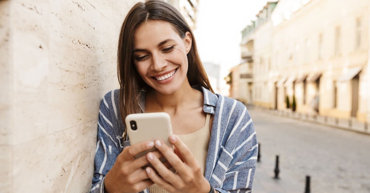 A smiling woman looking at her phone on a city street