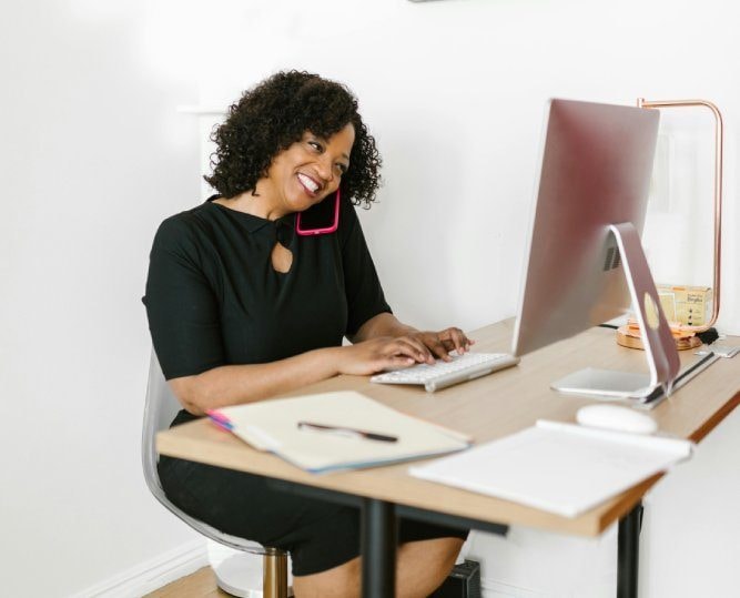A woman laughing as she works at a desktop computer in a bright office