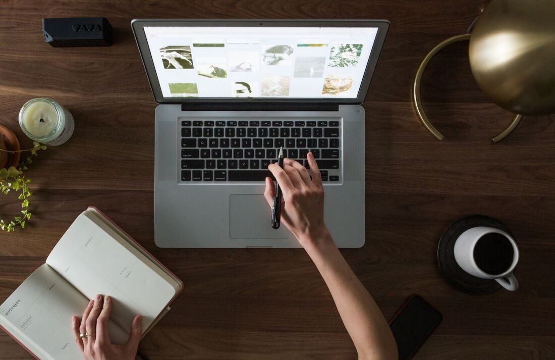 Overhead view of someone working on a laptop at a wooden desk with a notebook and a cup of coffee