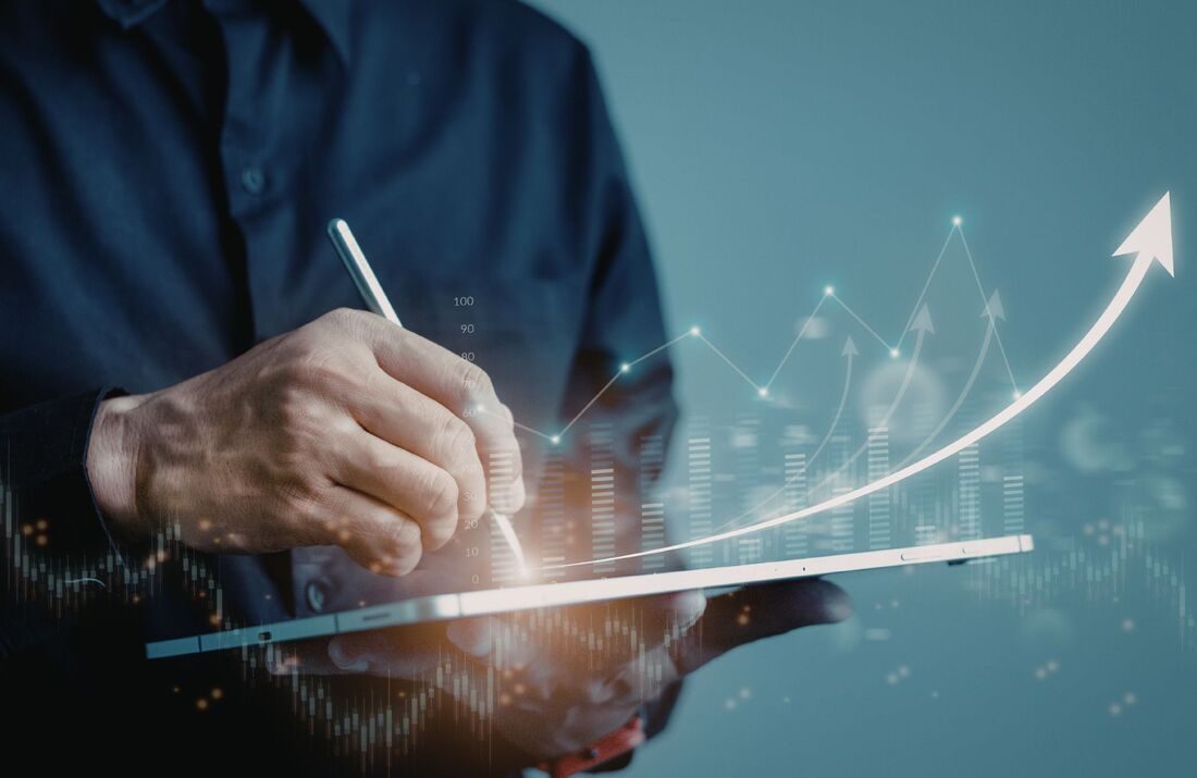 A hand with a stylus on a tablet showing a rising graph