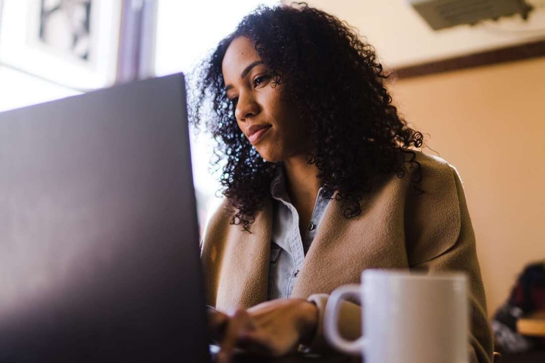 A woman with curly hair working on a laptop in a warm, softly lit room, a coffee mug in the foreground
