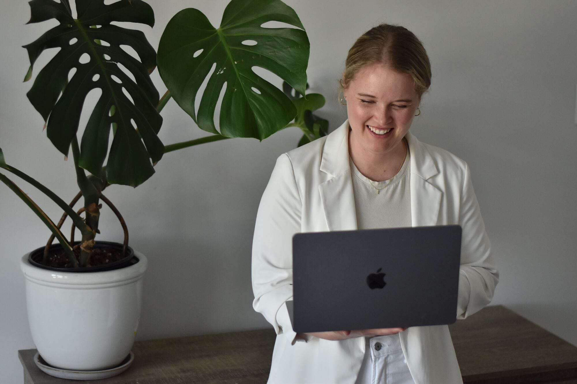 Jessica smiling at her laptop beside a monstera plant