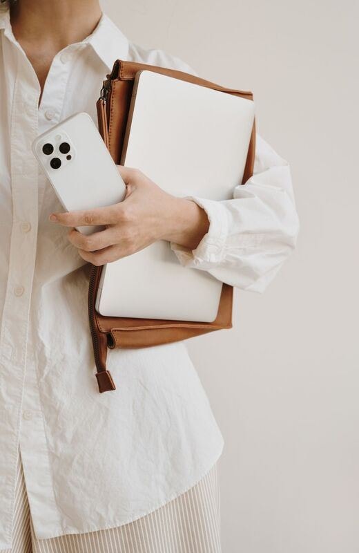 A laptop, a leather folio, and a phone held against a white linen shirt