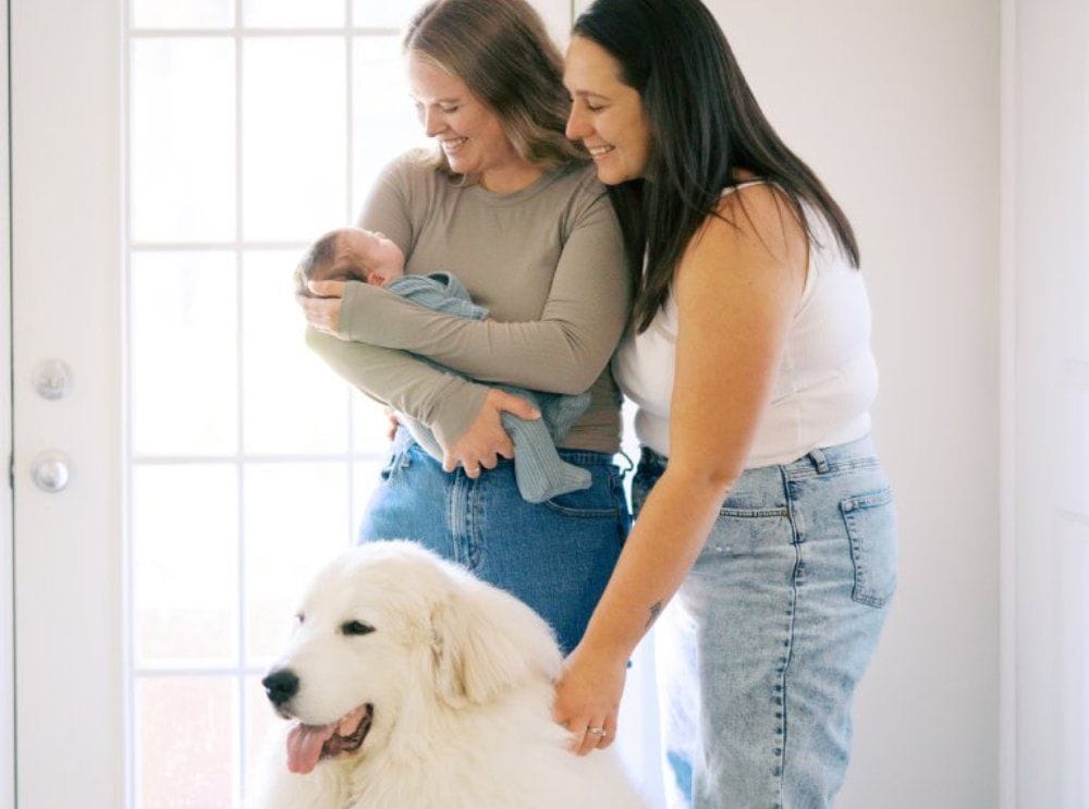 Jessica, her wife, and their baby daughter at home, with their Great Pyrenees