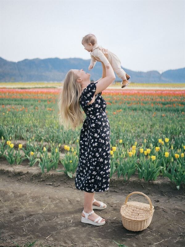 Jessica lifting her baby daughter up high in a tulip field, with mountains behind