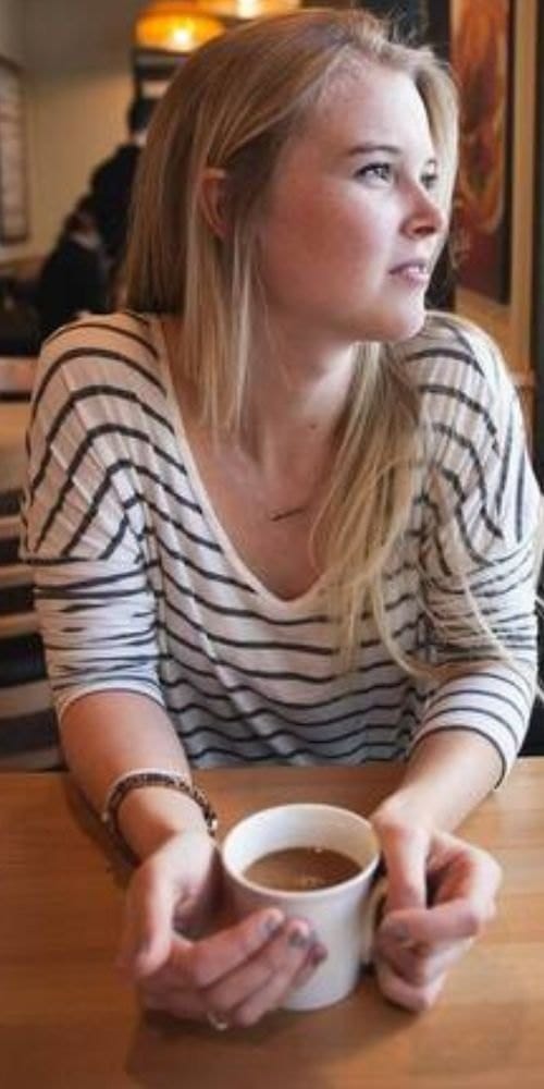Jessica holding a warm cup of coffee in a bright café