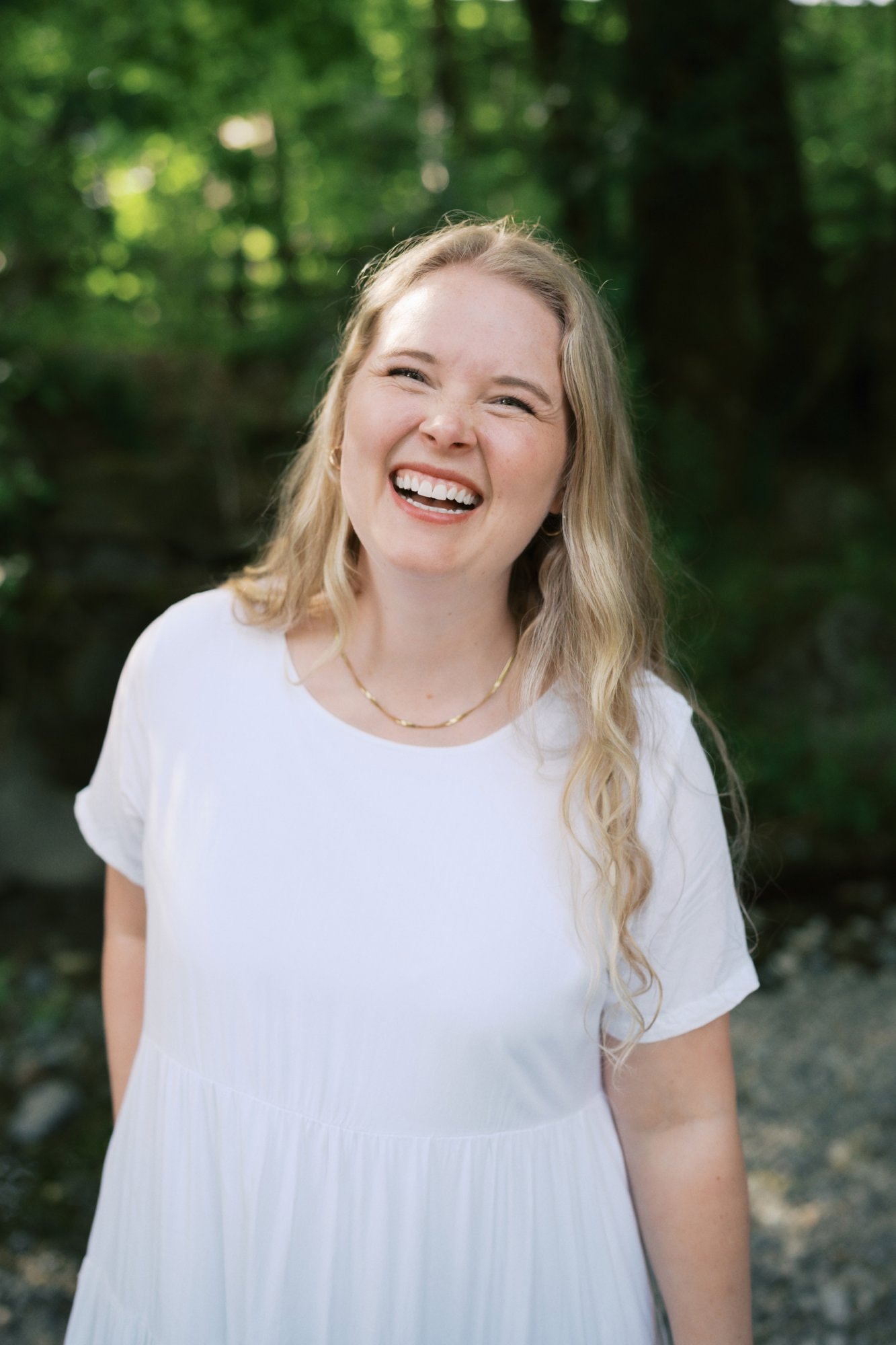 Jessica laughing outdoors in a white dress, with a leafy forest behind her